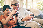 Family, fun and a boy gaming with his grandfather on a sofa in the living room of their home during a visit. Video game, children and a senior man learning how to play from his gamer grandson