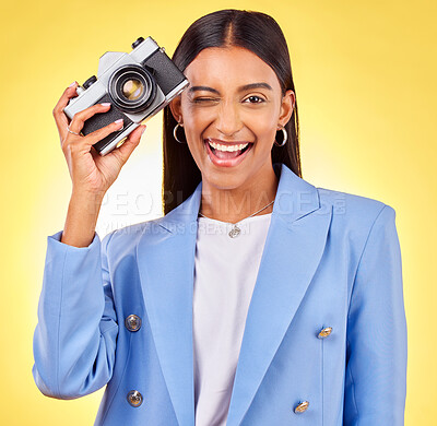 Buy stock photo Camera, photography and woman portrait with a smile and wink for picture in studio. Happy, female person and yellow background with creative, memory and funny emoji face with photographer skill