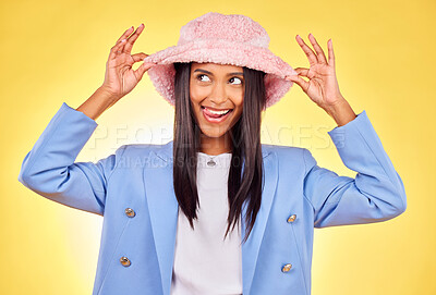Buy stock photo Fashion, funny face and hat with a trendy indian woman on a yellow background in studio for style. Comic, smile and accessories with a happy young model sticking out her tongue in a cute outfit