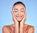 Skincare, peace and hands on face with happy woman in studio with blue background and dermatology or cosmetics. Indian, model and happiness with natural skin and healthy facial glow or beauty care