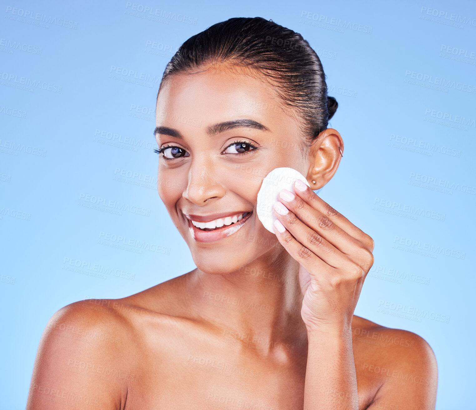 Buy stock photo Woman, face portrait and cotton pad for skincare, cosmetics and aesthetic glow on blue background in studio. Happy young indian model, facial cleaning and beauty of dermatology, shine and wipe makeup