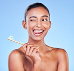 Wink, woman and brushing teeth in studio for dental wellness, care and smile on blue background. Happy indian model, bamboo toothbrush and cleaning mouth for fresh breath, oral hygiene and tongue out