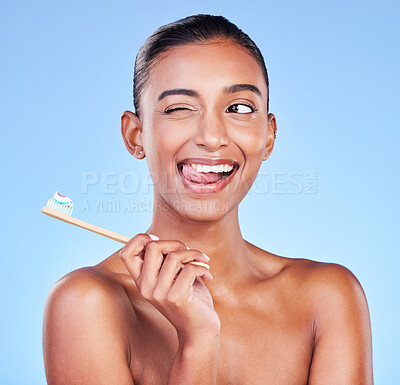 Buy stock photo Fun, woman or brushing teeth in studio for dental wellness, care or smile on blue background. Happy indian model, bamboo toothbrush or cleaning mouth for fresh breath, oral hygiene or tongue out wink