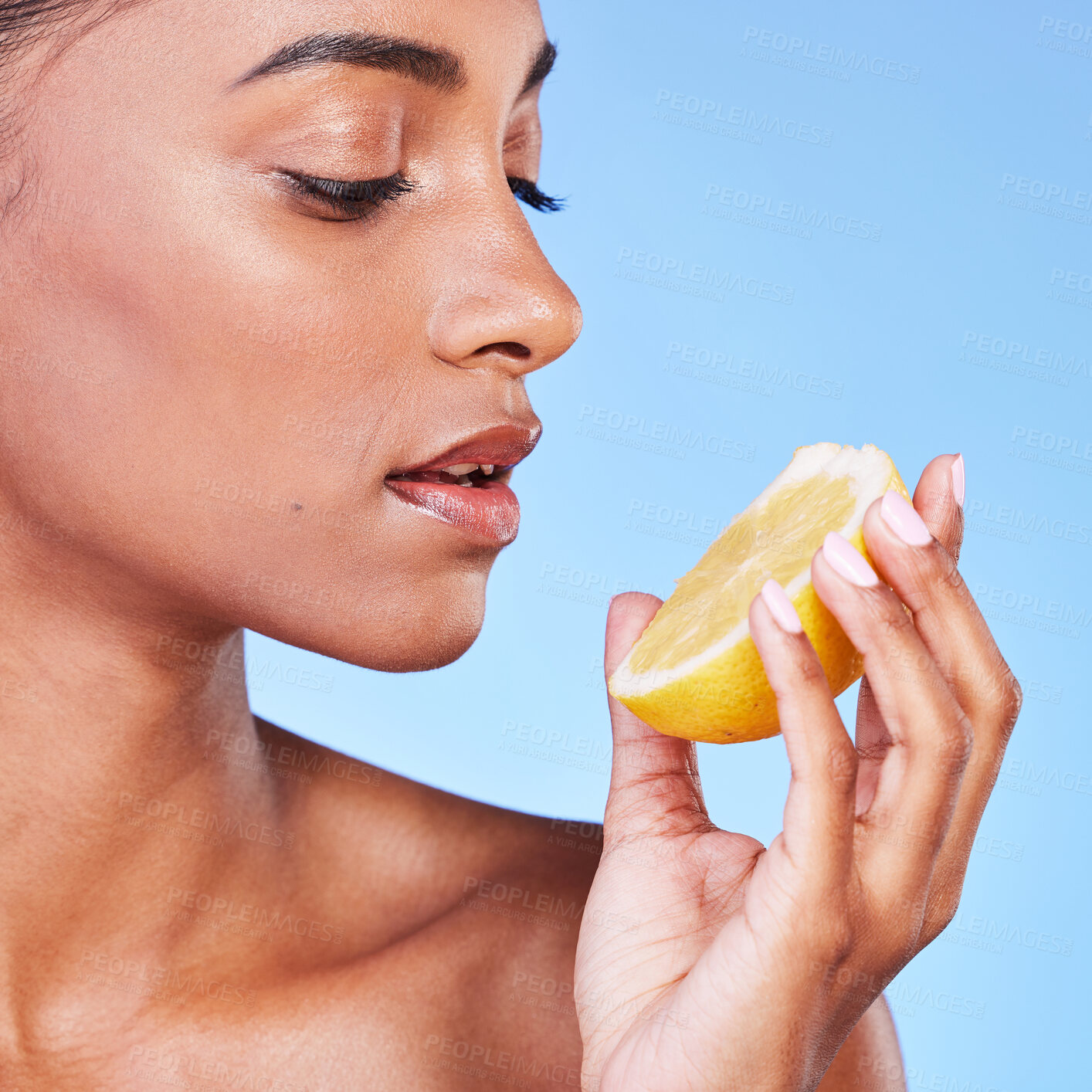 Buy stock photo Woman, face and lemon in studio for beauty, vitamin c cosmetics and natural nutrition. Indian model, healthy skincare and eating citrus fruits for vegan dermatology, mockup space and blue background