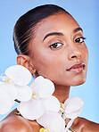 Flower, skincare and portrait of woman in studio for beauty, wellness and organic body care on blue background. Floral, face and Indian female model with petals for eco friendly dermatology or shine