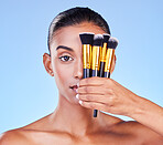 Woman, portrait and beauty, makeup brush on eye, foundation with cosmetics isolated on blue background, Indian model face, wellness and cosmetology with tools or equipment, skin and shine in studio