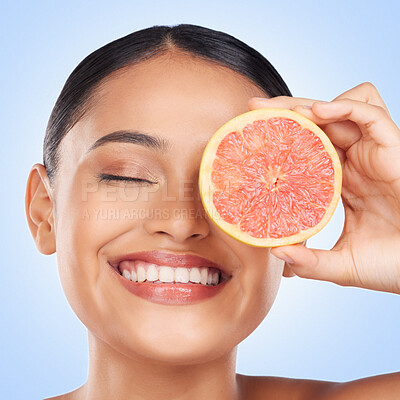 Buy stock photo Face, skincare and grapefruit with a natural woman in studio on a blue background for health or wellness. Beauty, smile and aesthetic with a happy young model holding fruit for detox or antioxidants