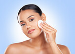 Woman, portrait and cotton in studio for skincare, cosmetics and facial aesthetic glow on blue background. Young model, cleaning pad and natural beauty for dermatology, shine and wipe makeup on face