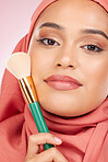 Cosmetics, brush and portrait of Islamic woman with makeup artist tools, beauty product and self care glow. Facial powder application, studio and hijab face of Arabic Muslim model on pink background