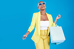 Fashion, deal and black woman in studio with shopping, bag and glasses, excited and smile on blue background. Retail, store and African female customer happy with boutique, discount and mall sale