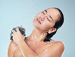 Woman, shower and water drops with loofah in hygiene, grooming or washing against a blue studio background. Female person in relax for body wash, cleaning or skincare routine under rain in bathroom
