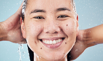 Buy stock photo Face, shower and happy woman cleaning hair in studio isolated on blue background. Water splash, hygiene and portrait of natural Asian model smile, washing or bathing for wellness, beauty and skincare