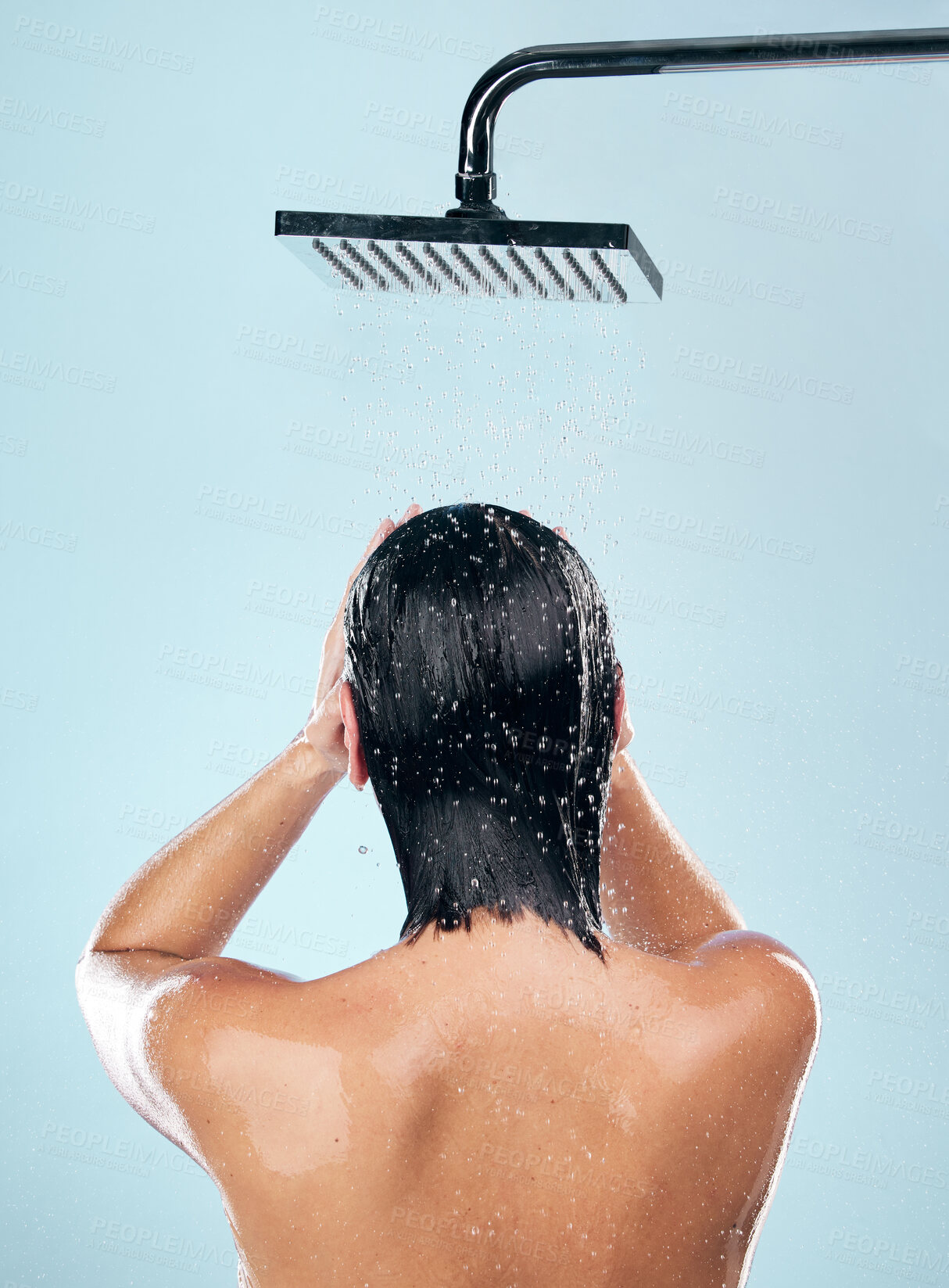 Buy stock photo Woman, shower and back in water drops for hygiene, grooming or washing against a blue studio background. Rear view of female person in body wash, cleaning or skincare routine under rain in bathroom