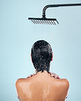 Woman, shower and back in water drops for washing, grooming or hygiene against a blue studio background. Rear view of female person in body wash, cleaning or skincare routine under rain in bathroom