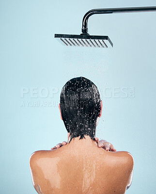 Buy stock photo Woman, shower and back in water drops for washing, grooming or hygiene against a blue studio background. Rear view of female person in body wash, cleaning or skincare routine under rain in bathroom