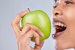 Apple, black woman and eating with health, diet and natural skincare glow in studio. Happy, face and fruit  closeup for healthy nutrition, grey background and balance with a smile from organic food