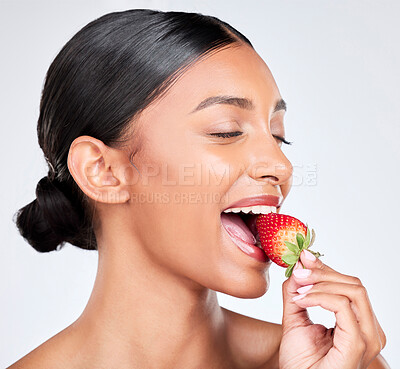 Buy stock photo Diet, happy and woman eating strawberry in studio for healthy organic snack for nutrition. Wellness, beauty and young Indian female model with fruit for natural skin detox routine by white background