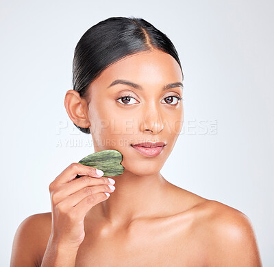 Buy stock photo Portrait, skincare and gua sha facial massage with a woman in studio on white background holding a stone. Face, beauty and natural with a confident young model using antiaging jade to relax her skin