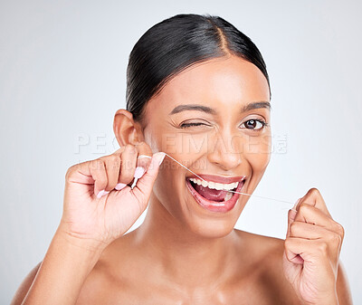 Buy stock photo Woman, portrait and wink to floss teeth in studio for healthy dental care, gum gingivitis or plaque on white background. Face, happy indian model and oral thread for cleaning mouth, tooth and hygiene