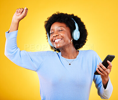 Buy stock photo Happy black woman, phone and headphones listening to music against a yellow studio background. African female person smile, afro or mobile smartphone app dancing to audio track, sound or podcast
