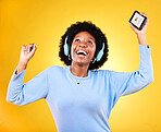 Happy black woman, phone and headphones for music listening against a yellow studio background. African female person smile, afro or mobile smartphone app dancing to audio track, sound or podcast