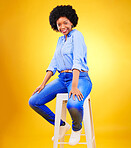 Happy, portrait and black woman on chair with fashion, casual style and natural confidence on yellow background in studio. Face, smile and African person with afro, pride and beauty from cosmetics