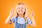 Child, fingers crossed and wish or hope in studio for luck, prayer or faith. Face of excited young girl kid on a orange background for hand gesture, icon or sign for dream, optimistic or superstition