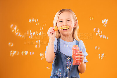 Buy stock photo Portrait, happy child and blowing bubbles in studio for fun, freedom and childhood development on orange background. Girl, kid and smile for playing with soap bubble wand, toys and activity games