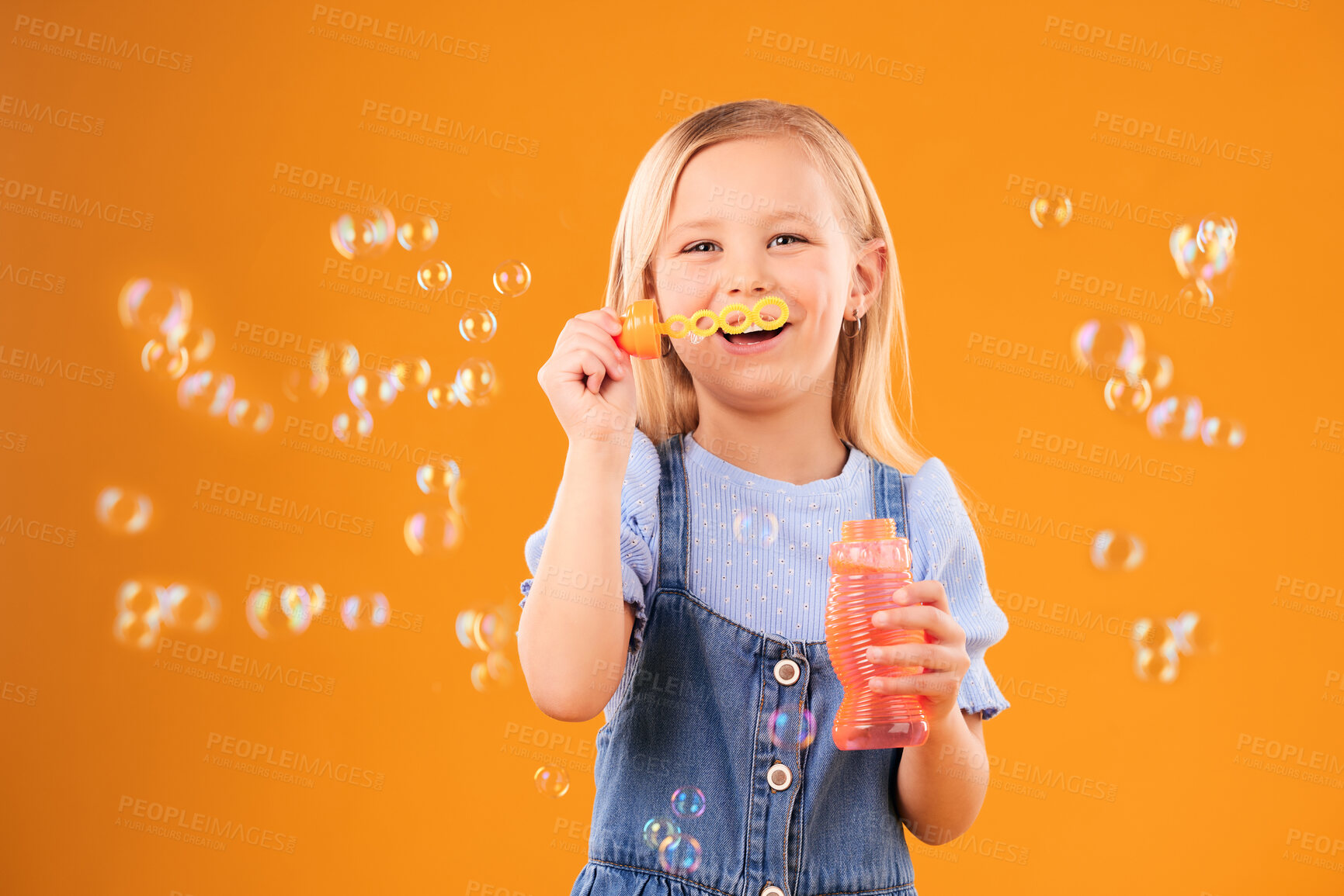 Buy stock photo Portrait, happy child and blowing bubbles in studio for fun, freedom and childhood development on orange background. Girl, kid and smile for playing with soap bubble wand, toys and activity games