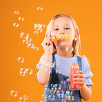 Portrait, child and blowing bubbles in studio for fun, freedom and childhood development on orange background. Young girl, kid and learning to play with soap bubble wand, toys and activity games