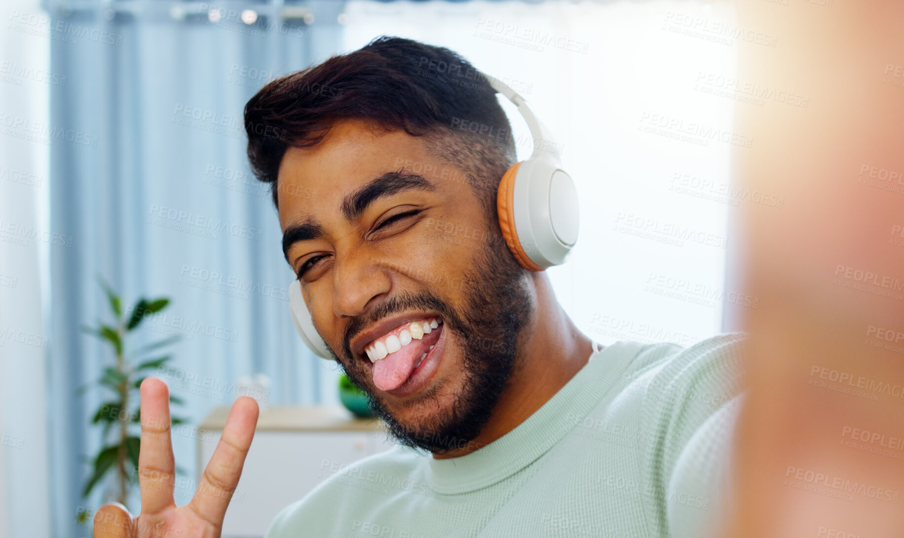 Buy stock photo Selfie, man and smiling tongue out emoji headphones for music playlist streaming and cheerful mood in home. Wellness peace sign, audio and happy male ready to dance photograph with smile.