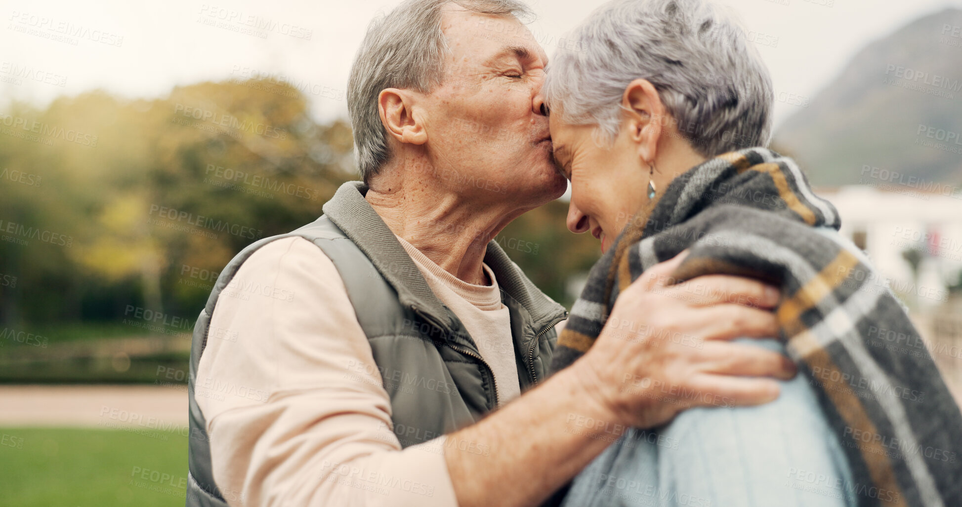 Buy stock photo Forehead, kiss and senior couple in a park with love, happy and conversation with romantic bonding. Kissing, old people and elderly man embrace woman with care, romance or soulmate connection outdoor
