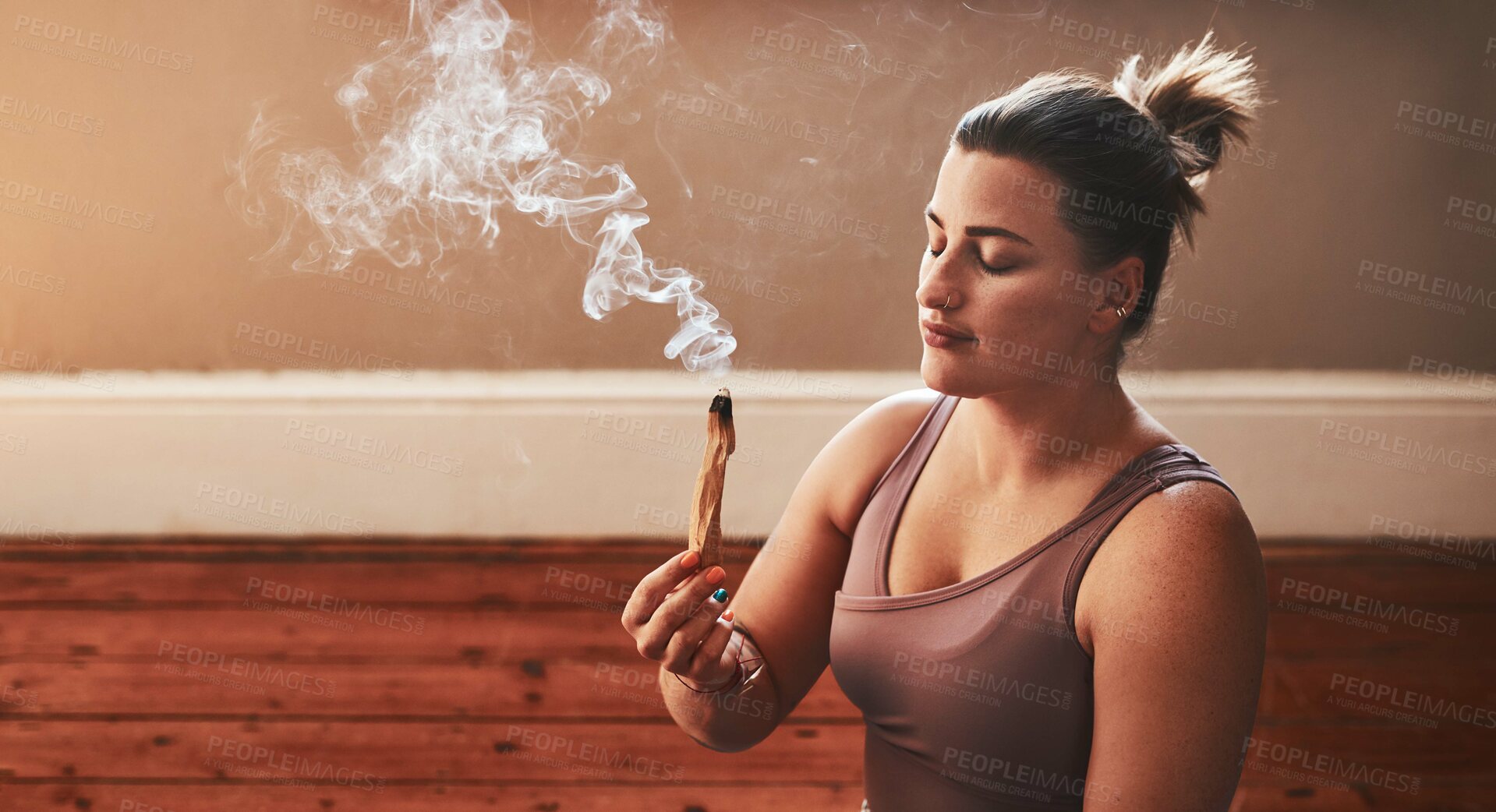 Buy stock photo Shot of a young woman burning a palo santo stick at home