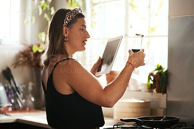 Buy stock photo Shot of a young woman using a digital tablet and reading the label on a bottle while preparing a meal