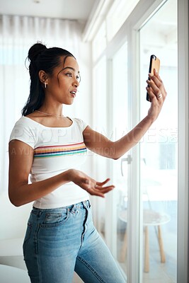 Buy stock photo Cropped shot of an attractive young blogger standing in her home and using her cellphone to record a vlog
