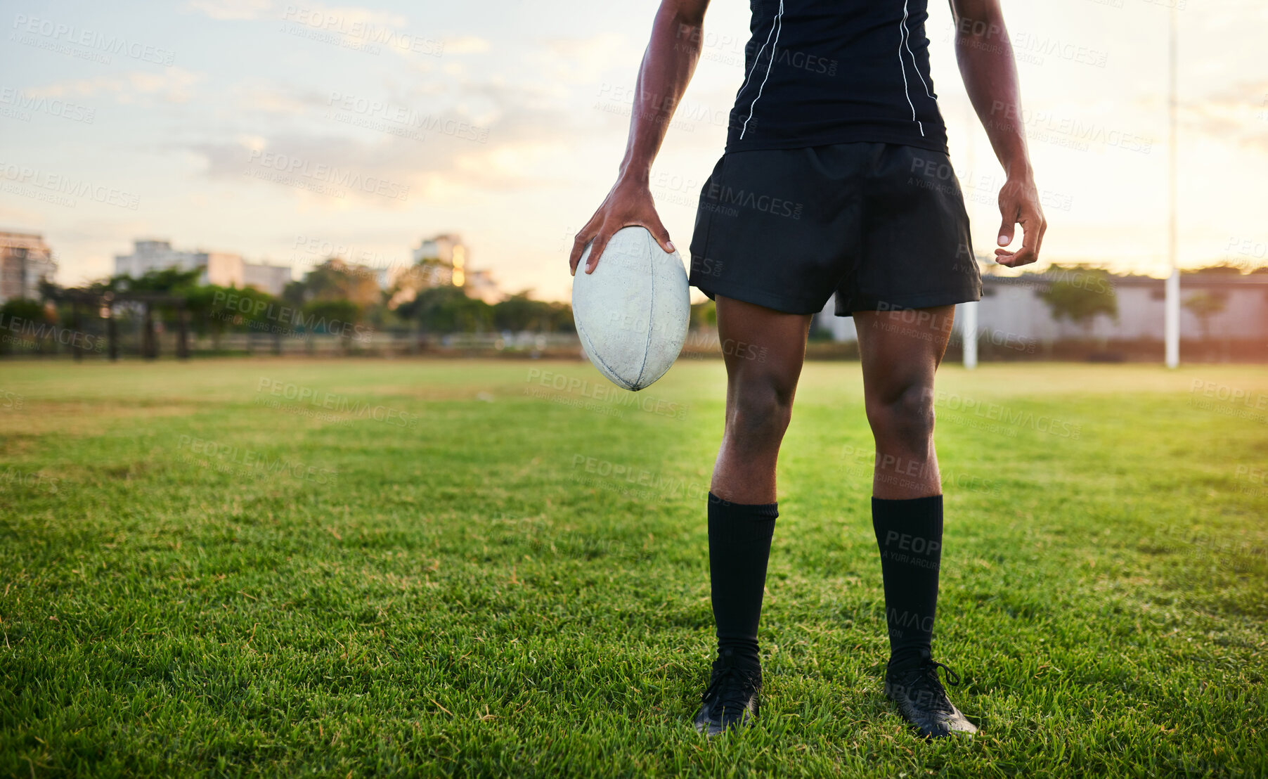 Buy stock photo Cropped shot of an unrecognizable sportsman standing alone and holding a rugby ball during a morning practice