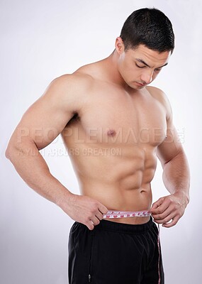 Buy stock photo Shot of a young muscular man measuring his waist against a grey studio background