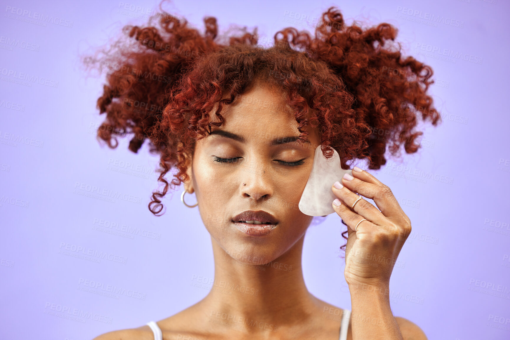 Buy stock photo Face, gua sha and skincare, woman and beauty with cosmetic tools isolated on purple background. Red hair, curls and facial massage with stone, dermatology and wellness with skin glow in a studio