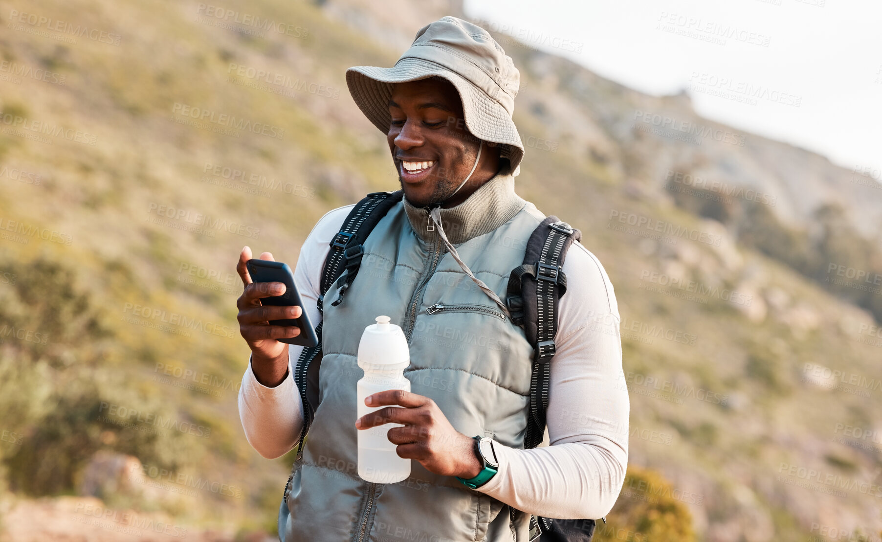 Buy stock photo Hiking, water bottle and black man with a cellphone, smile or hydration with fitness, travel or health. African person, guy or hiker with a smartphone, mountain or thirsty with exercise or connection