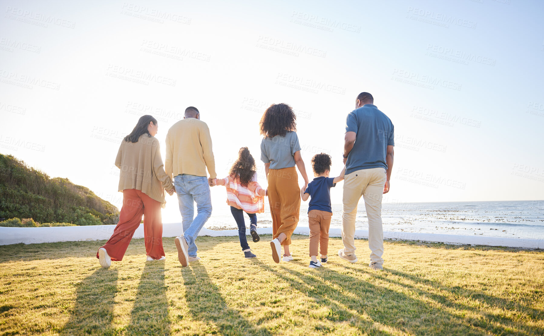 Buy stock photo Nature, walking and back of big family holding hands, unity solidarity or bond on wellness holiday, travel or love. Sunshine flare, sky and relax kids, mom and dad support, trust and journey on grass