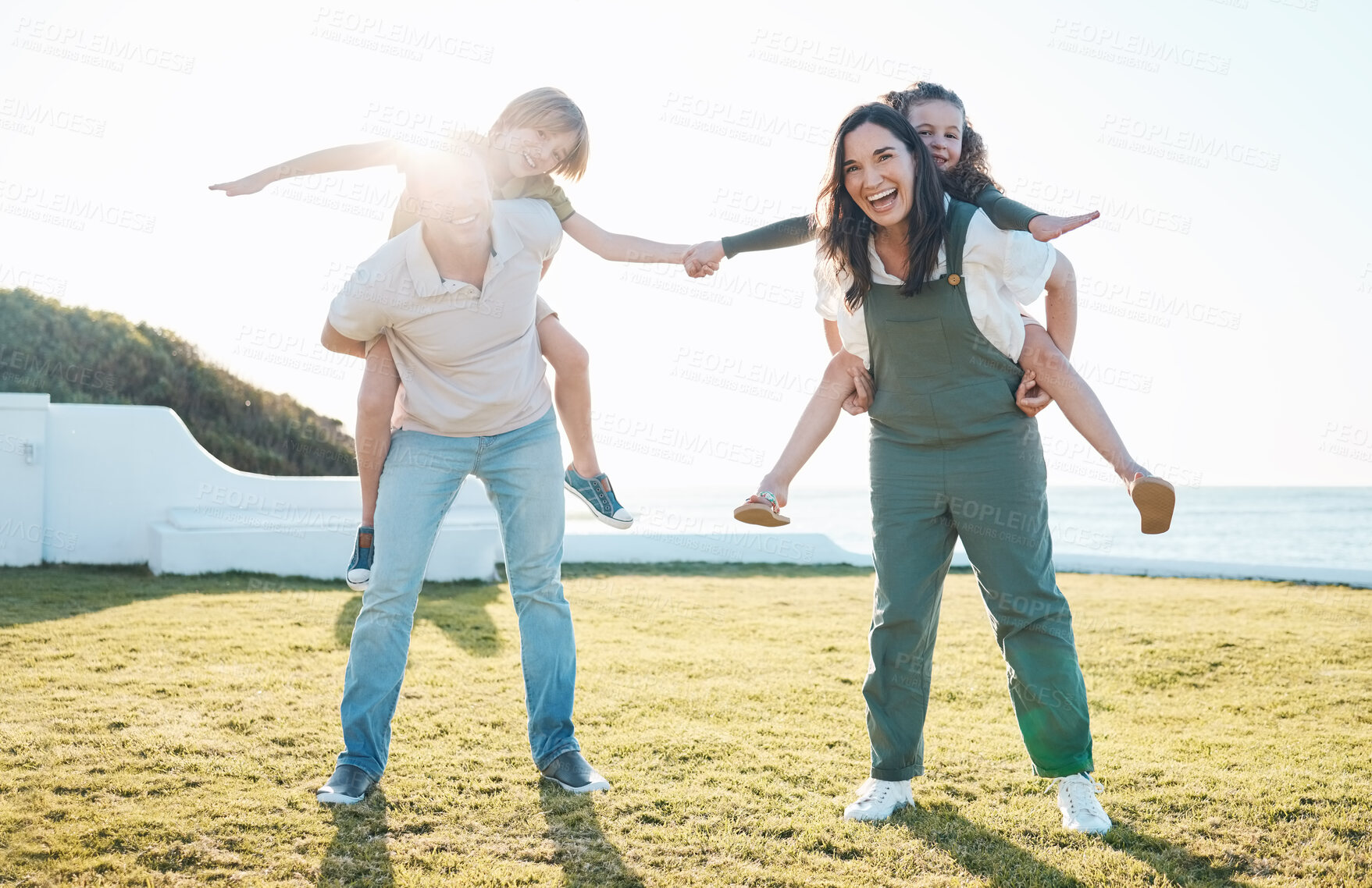 Buy stock photo Family, parents and portrait of children on grass by ocean for bonding, relationship and relax together. Nature, travel and happy mother, father carrying kids on holiday, summer vacation and playing