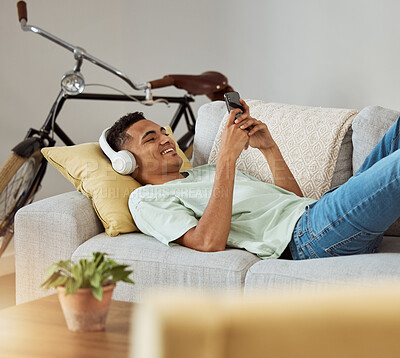 Buy stock photo Headphones, phone video and relax man on a living room sofa happy at home. Series, funny app and laughing with music and listening in a house lounge with web mobile streaming and couch with smile