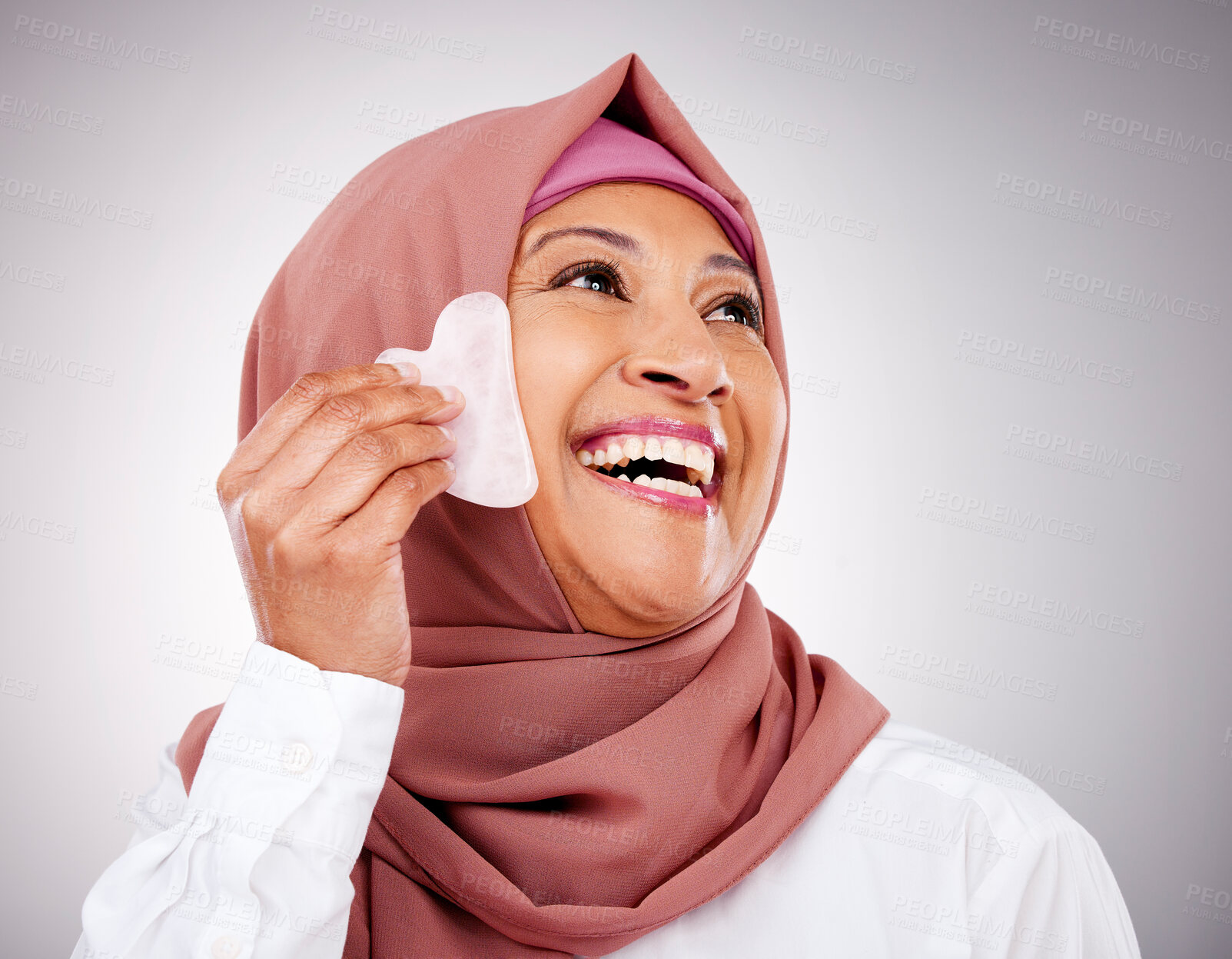 Buy stock photo Skin, gua sha stone and a muslim woman closeup in studio on a gray background for beauty. Skincare, smile and natural with a happy mature arab person massaging her face for antiaging treatment