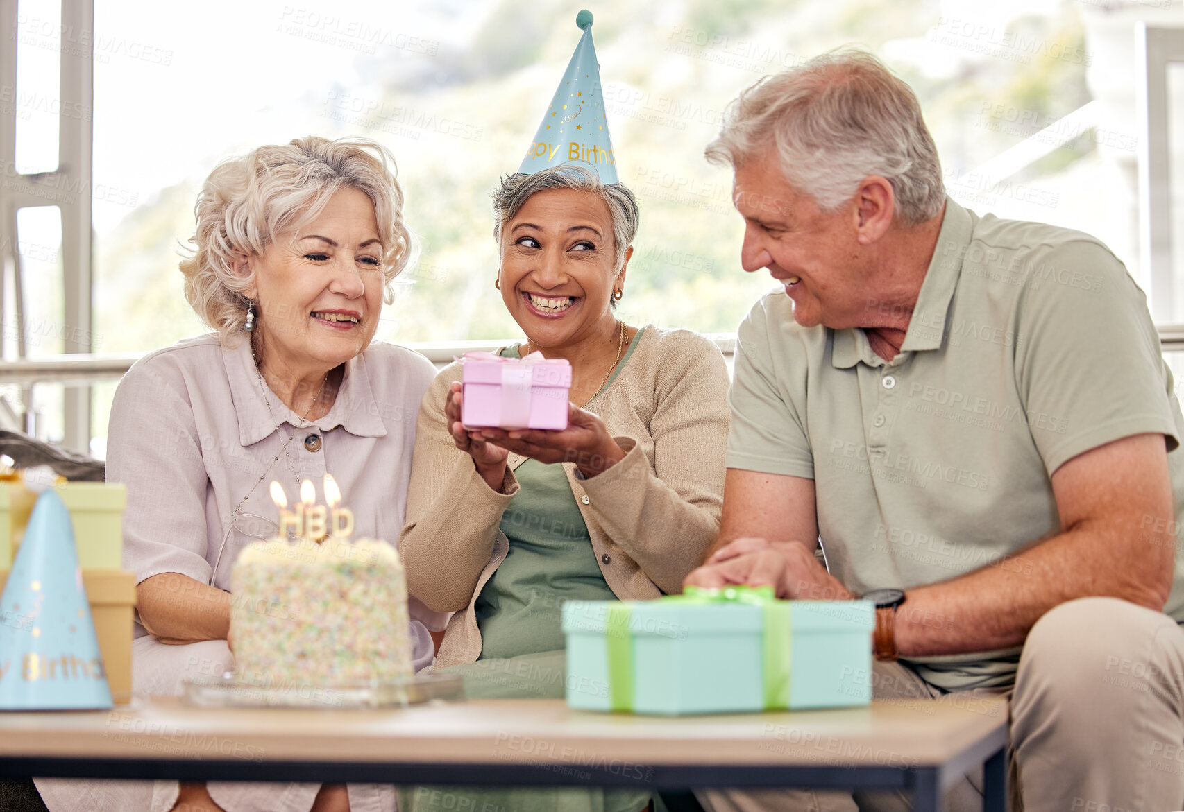 Buy stock photo Birthday, senior friends with cake and gift for celebration in living room, smile and candles in retirement. Happiness, old people and party with dessert, surprise and elderly man with women on sofa.