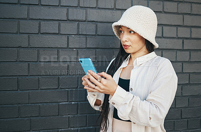 Buy stock photo Woman with phone, wall background and streetwear, typing social media post, chat or internet search. Urban fashion, gen z girl or online influencer with smartphone for content creation and technology