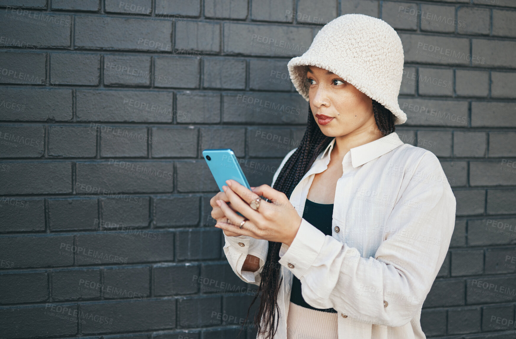 Buy stock photo Woman with phone, wall background and streetwear, typing social media post, chat or internet search. Urban fashion, gen z girl or online influencer with smartphone for content creation and technology