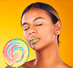 Beauty, lollipop and woman with makeup, candy and sprinkles on her lips on yellow studio background. Person, girl or model with sweet treats, aesthetic and dessert with mockup space or colorful snack