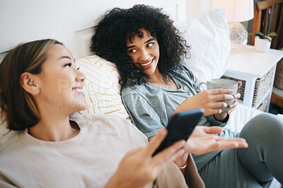 Buy stock photo Phone, coffee and lesbian couple on bed in conversation for bonding, relaxing and resting together. Happy, communication and young lgbtq women networking on cellphone with latte in bedroom at home.