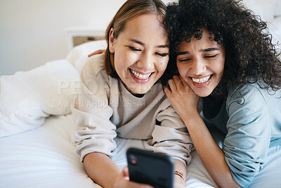 Buy stock photo Cellphone, relax and young lesbian couple in bed networking on social media, mobile app or the internet. Happy, technology and interracial lgbtq women scroll on a phone in bedroom at modern apartment