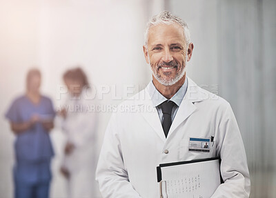 Buy stock photo Portrait of a mature male doctor standing in a hospital with his colleagues in the background